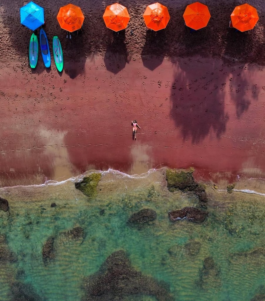 Foto aérea de mulher deitada na areia vermelha da Praia do Forno em Búzios